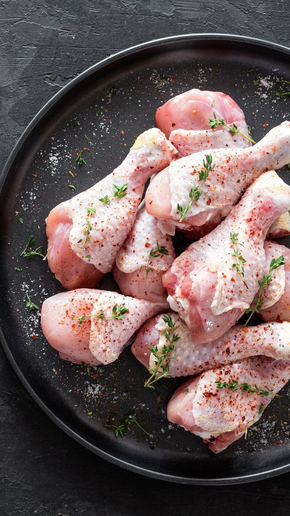 chicken_drumsticks Raw chicken drumsticks seasoned with spices and fresh thyme on a black plate, ready for cooking.